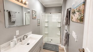 A modern bathroom with a large mirror, a white sink, a glass shower enclosure, and a towel rack. - Beautiful Escape-Sleeps 12-Patio-Games-Relax (Sumter)