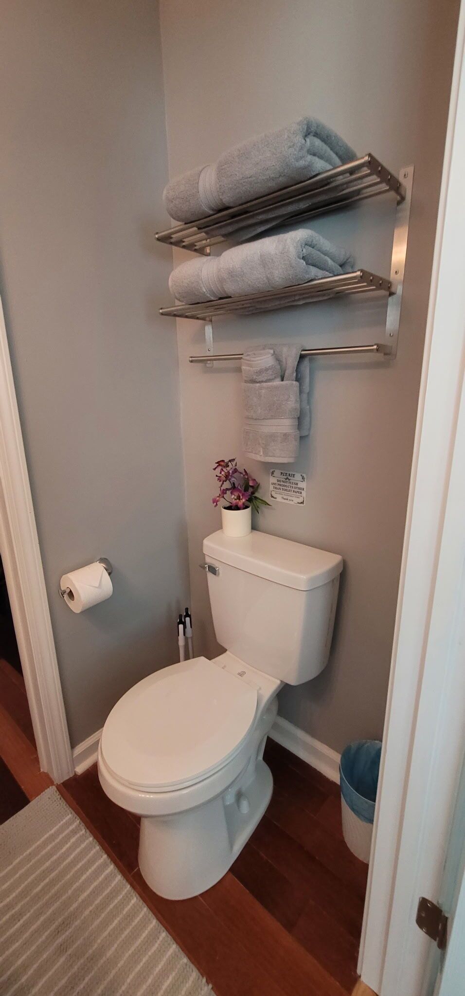 Et badeværelse med toilet, håndklædestang, toiletpapirholder og et skilt på væggen.