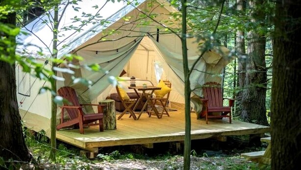 A tent with a table and chairs inside, surrounded by trees.