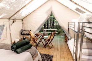 A tent with a wooden table and chairs, bunk beds, and a view of the forest.