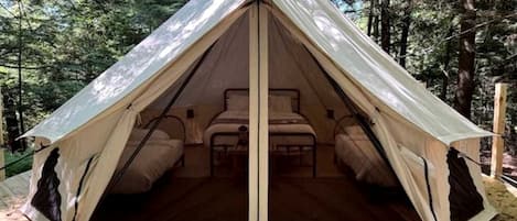A dome-shaped tent with a central bed and two side beds, set in a forest.