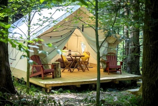 A tent with a table and chairs inside, surrounded by trees.