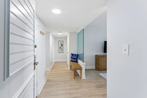A hallway with a bench, a framed picture on the wall, and a television on the right. - 1372 Shipwatch Oceanfront Beautifully Updated (Fernandina Beach)