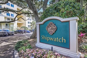 A sign with 'Shipwatch' written on it, surrounded by greenery and parked cars. - 1372 Shipwatch Oceanfront Beautifully Updated (Fernandina Beach)