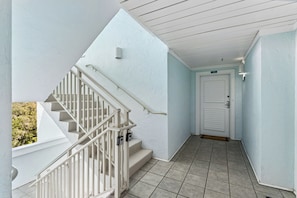 A staircase leading to a landing with a white door and a light blue wall. - 1372 Shipwatch Oceanfront Beautifully Updated (Fernandina Beach)