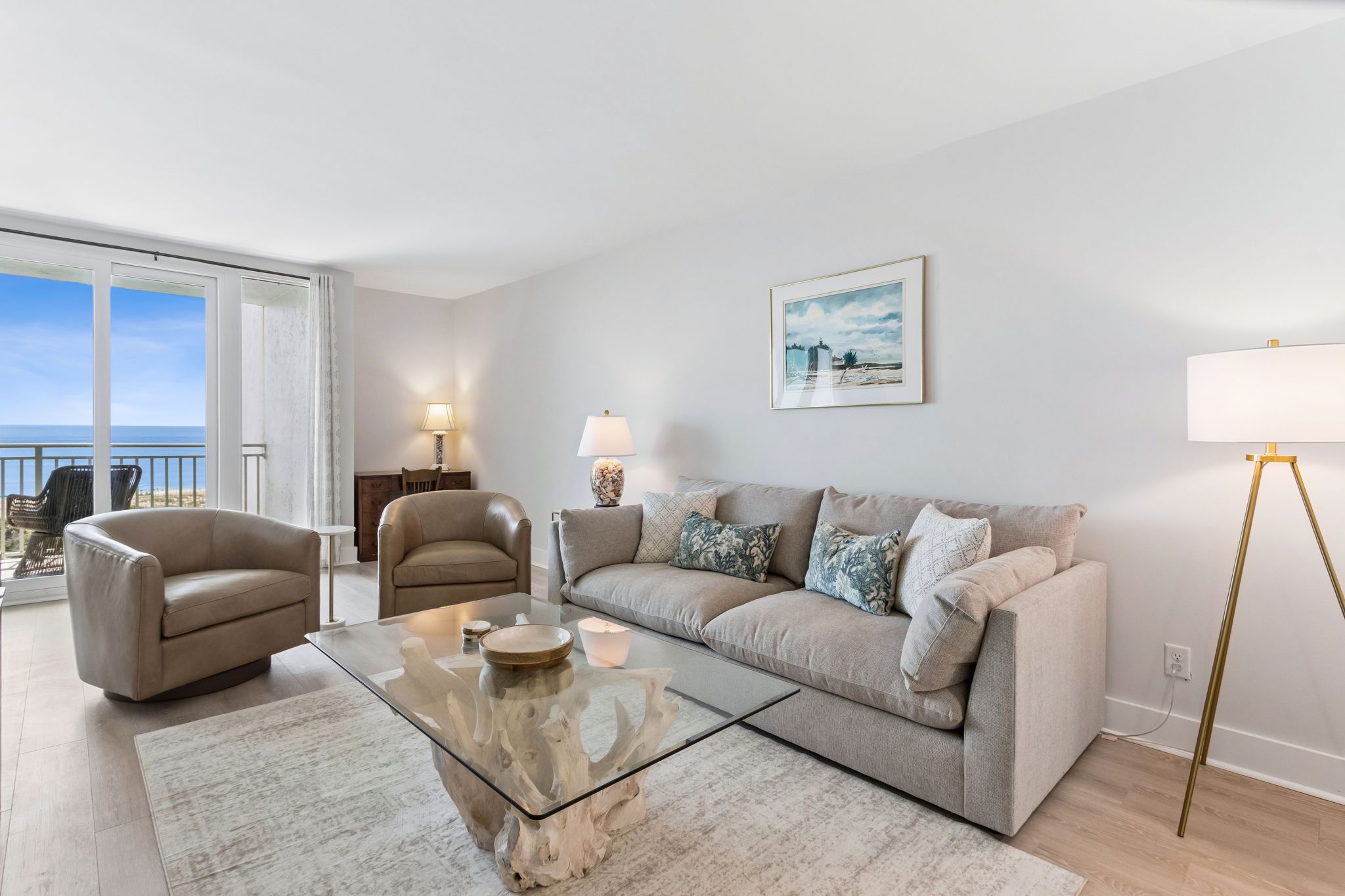 A modern living room with a sofa, armchairs, a glass coffee table, and a lamp.