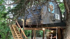 Ein Baumhaus mit einer Holztreppe, einer Hängematte und einer kleinen Sitzecke im Freien.
