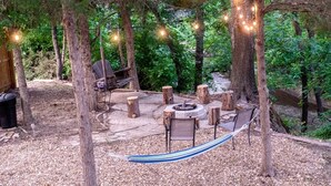 Un espace extérieur aménagé avec un foyer, des chaises en bois, un hamac et des guirlandes lumineuses.
