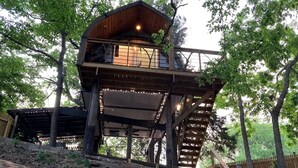 Ein Baumhaus aus Holz mit einem Balkon, umgeben von Bäumen und einer Holztreppe.