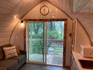 Interior acolhedor de cabana, com teto de madeira, porta de vidro corrediça que dá para um deck externo, uma mesa pequena e um micro-ondas.