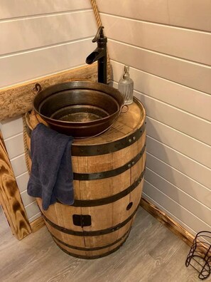 Uma pia de barril de madeira com uma torneira e um recipiente de vidro.