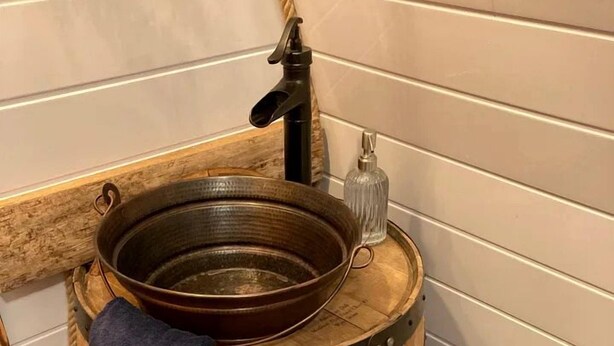 Ein Waschbecken aus Holzfass mit Wasserhahn und einem Glasbehälter.