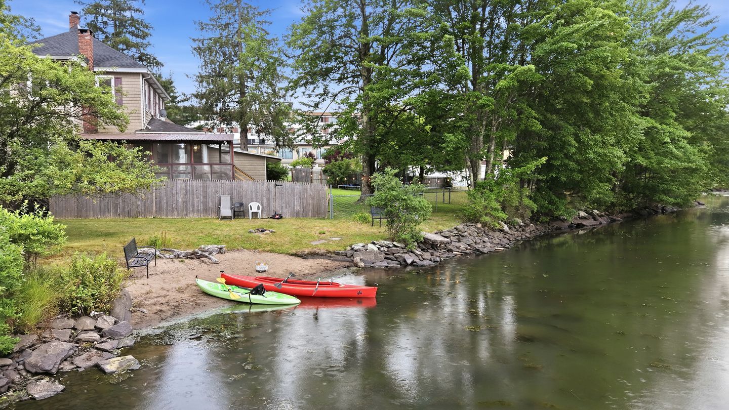 A riverside property with a house, kayaks, and a dock.
