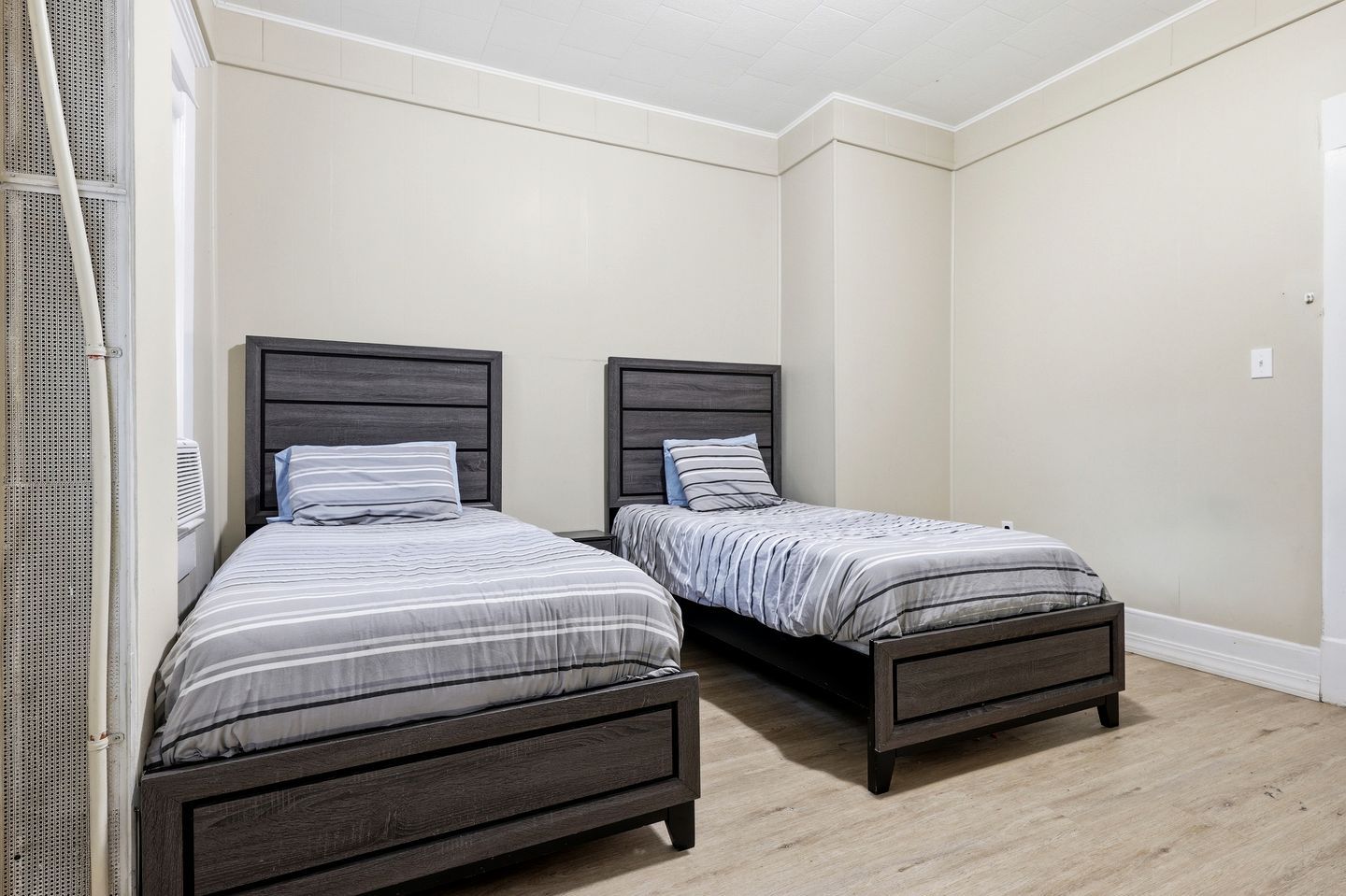 A room with two single beds, each with a wooden headboard and striped bedding.