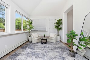 Una habitación con interior blanco, una mesa redonda con dos sillas y plantas en macetas.