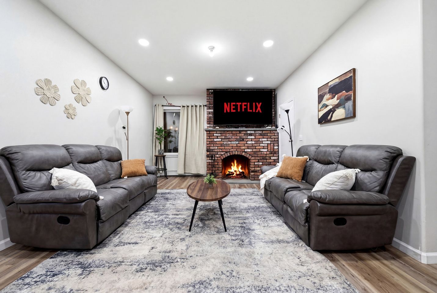 A modern living room with two leather sofas, a coffee table, a fireplace, and a wall-mounted TV displaying 'NETFLIX'.