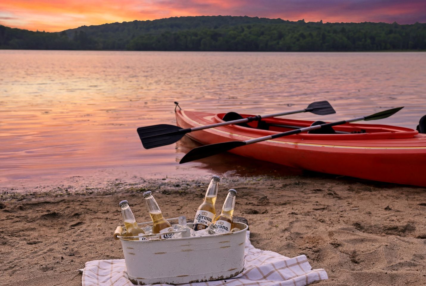 A kayak and bottles on a sandy beach with a lake and hills in the background.
