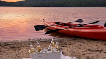 A kayak and bottles on a sandy beach with a lake and hills in the background.