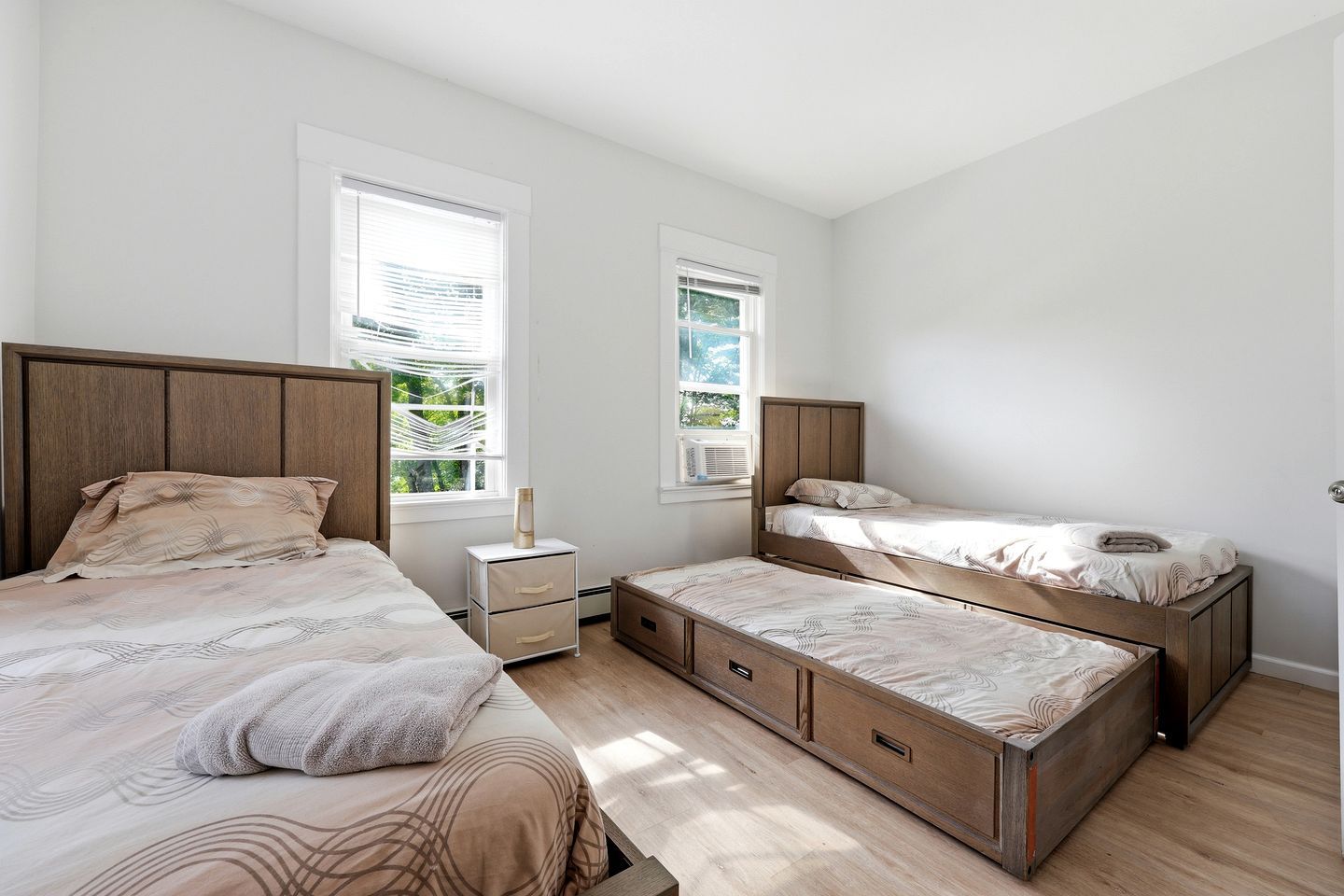 A bedroom with two beds, a nightstand, and a window.