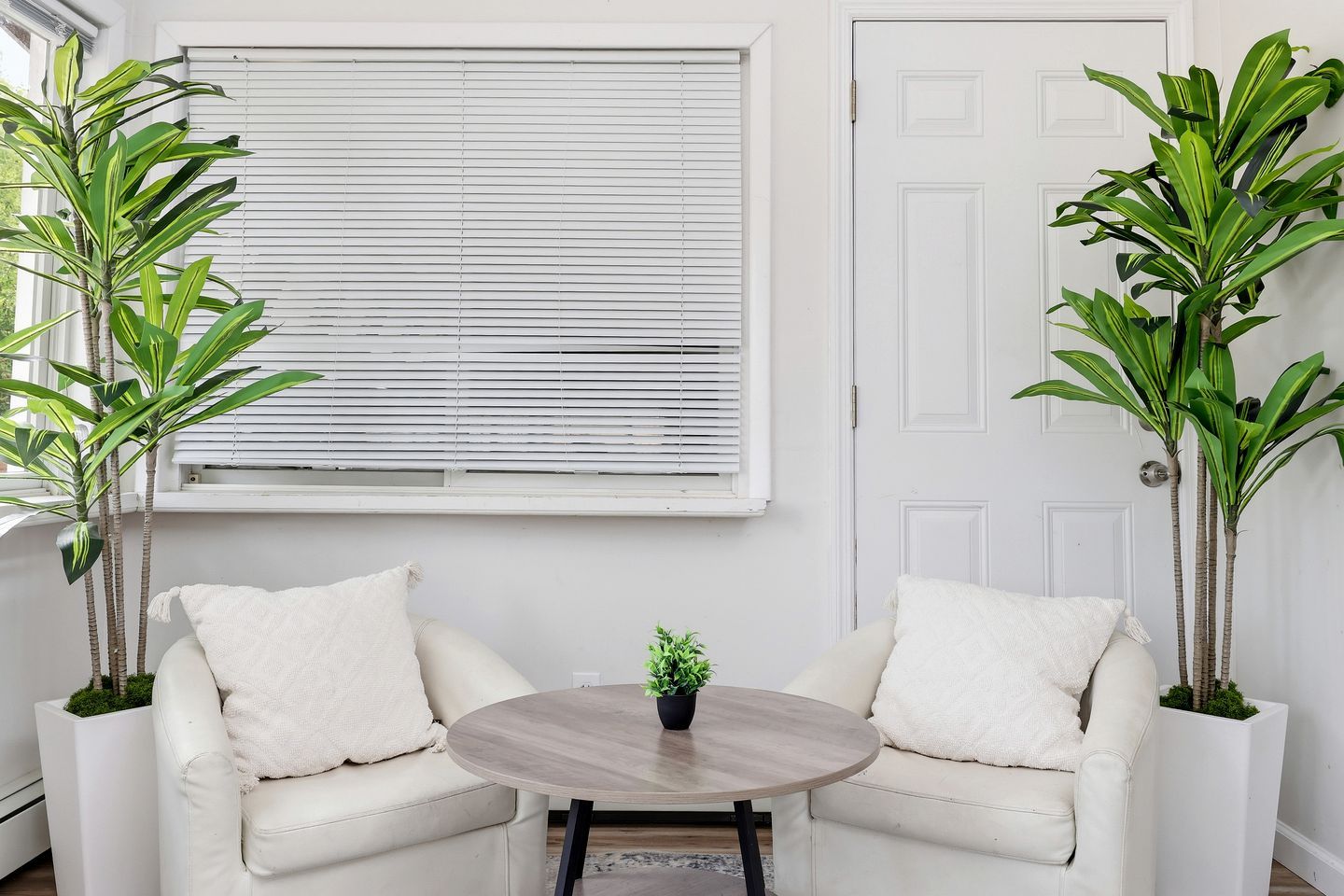 Una habitación con dos sofás blancos, una mesa redonda de madera y dos plantas en macetas.