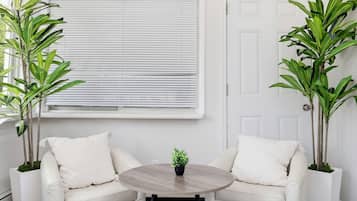 Una habitación con dos sofás blancos, una mesa redonda de madera y dos plantas en macetas.