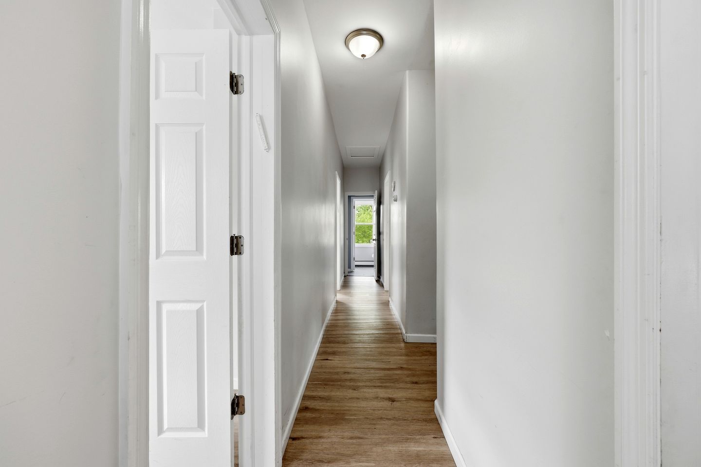 A hallway with white walls and wooden flooring leading to a door at the end.