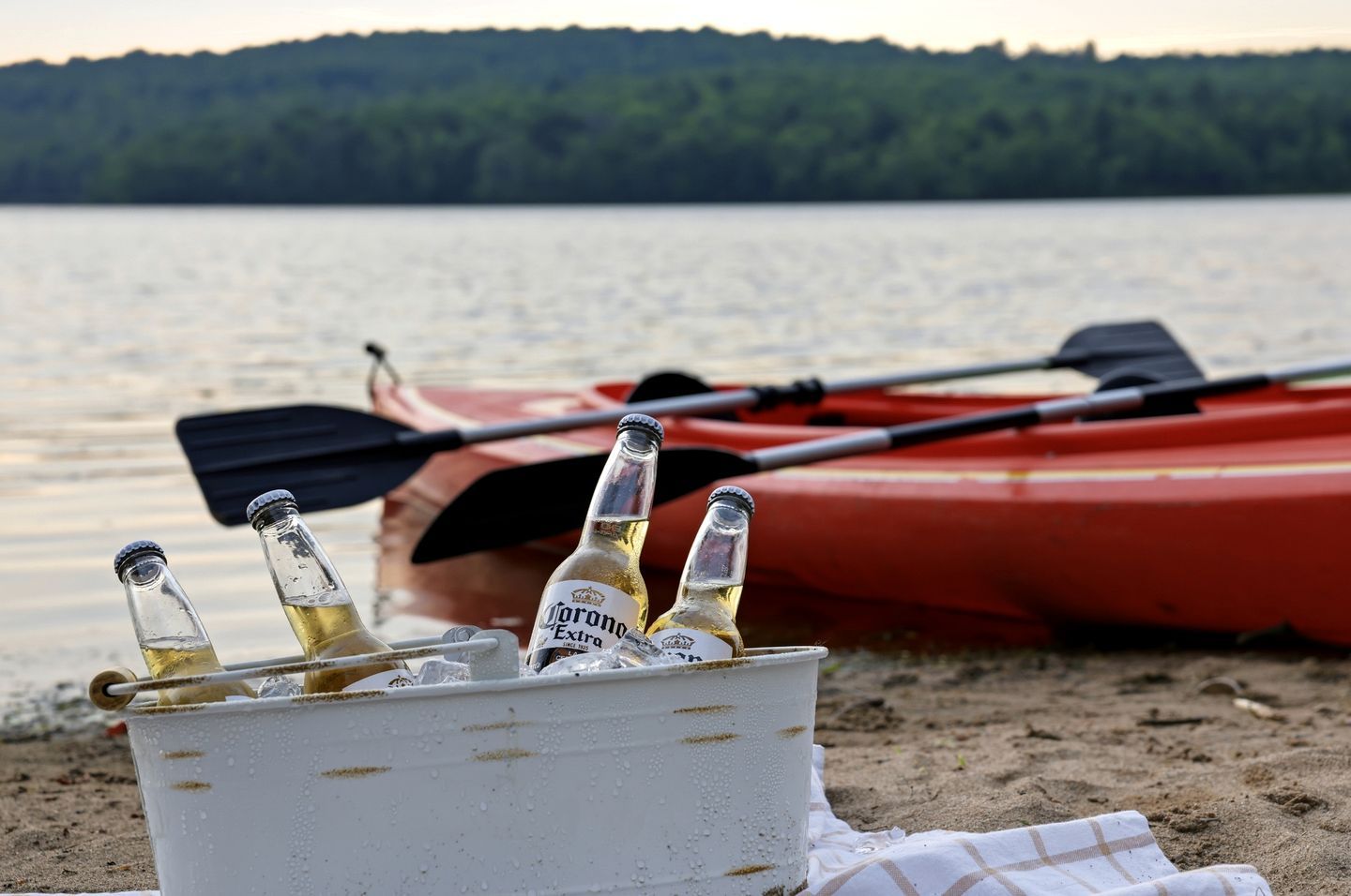 Cena de praia com um caiaque e um balde com garrafas de cerveja Corona Extra.