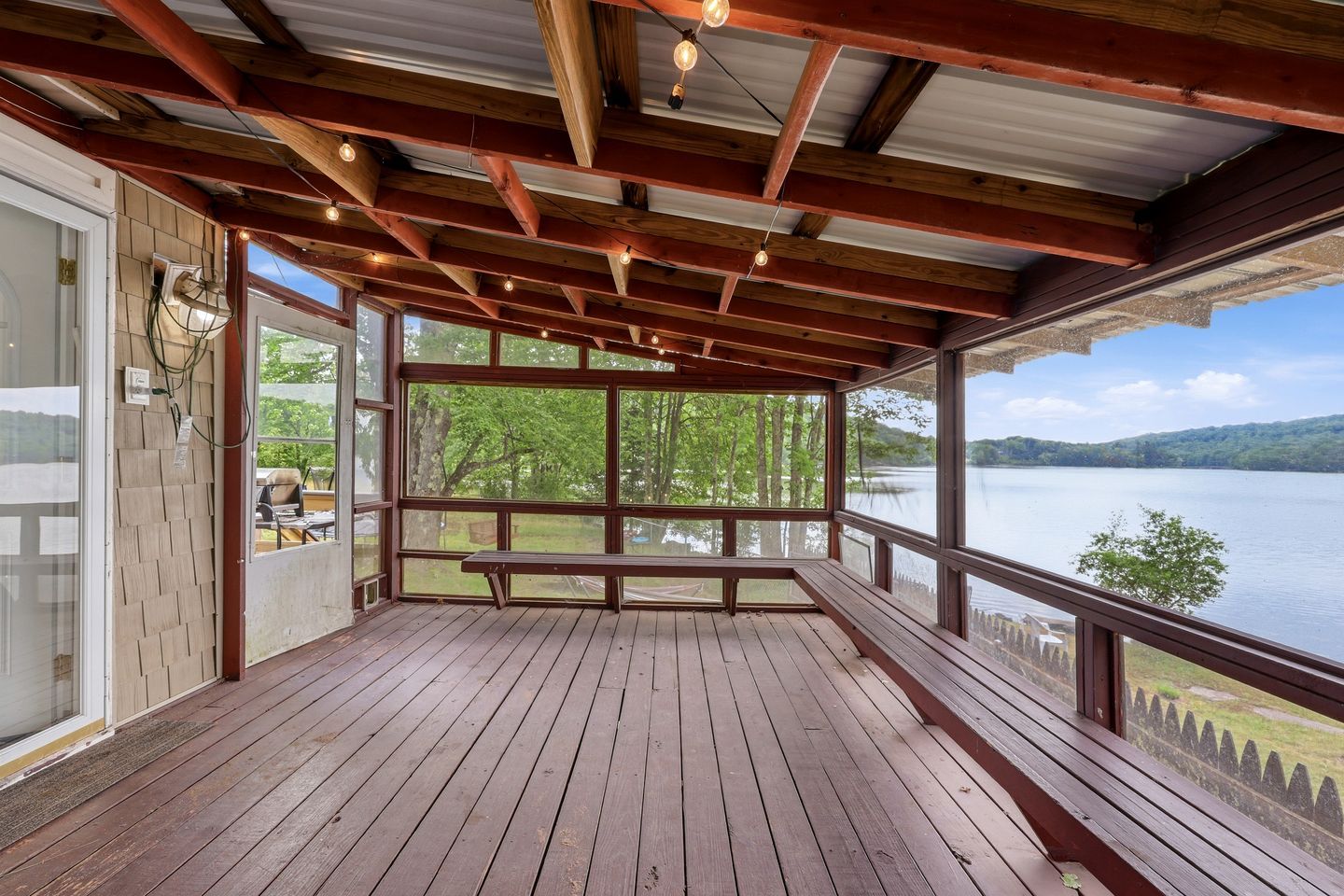 Une terrasse en bois avec un banc, de grandes fenêtres et une vue sur un lac.