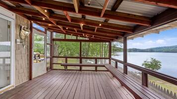 Une terrasse en bois avec un banc, de grandes fenêtres et une vue sur un lac.