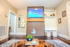 A living room with a flat-screen TV displaying Disney+, a bird sculpture, a potted plant, and a patterned rug. - Centrally Located King Bed Midtown Liberty 2697 (Memphis)