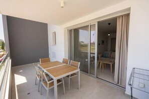 Un balcon avec une table et des chaises, une porte-fenêtre coulissante donnant sur un espace de vie et un étagère en métal.