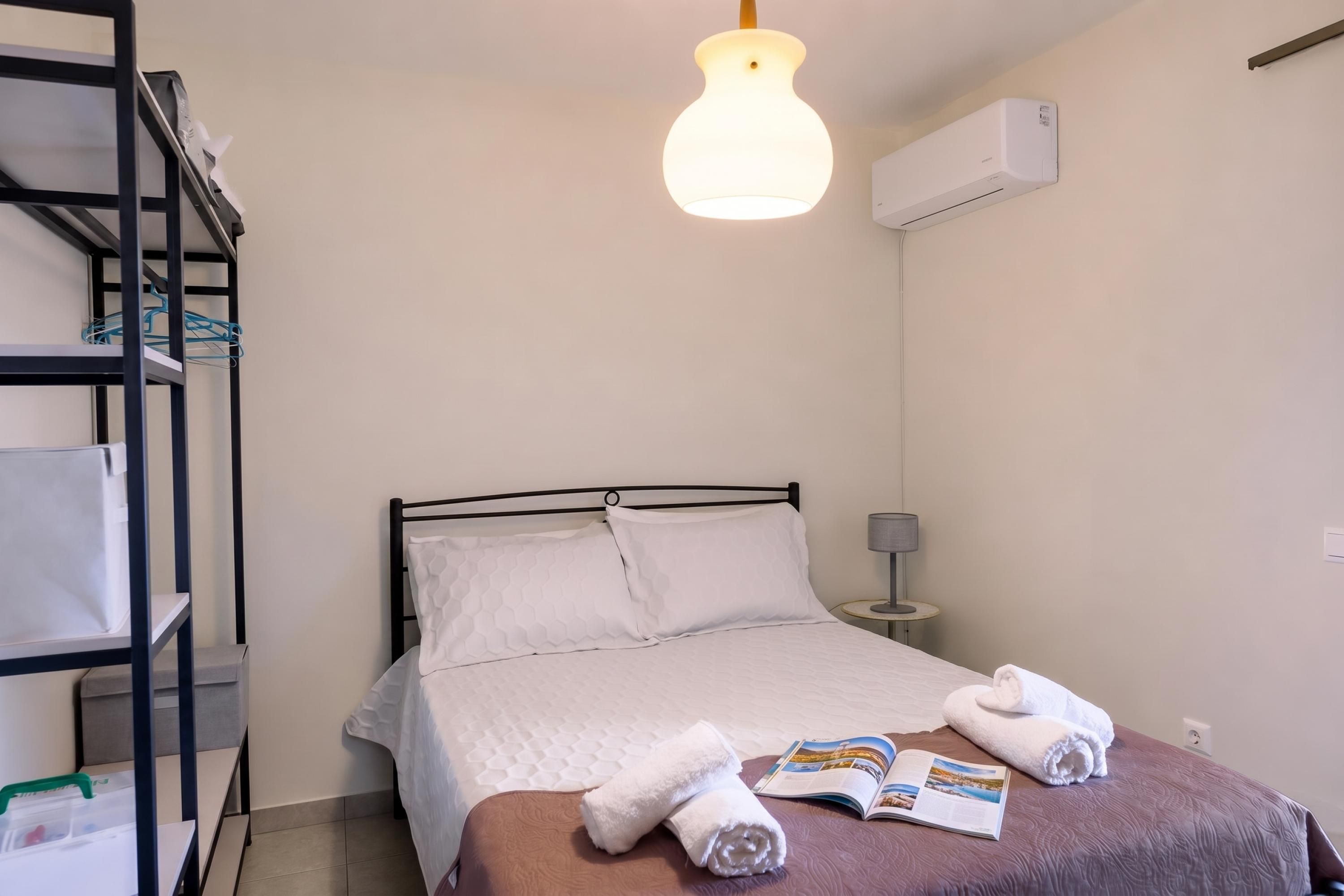 Ein Hotelzimmer mit einem Bett, einem Nachttisch, einer Lampe, einem Regal mit Handtüchern und einer Klimaanlage.