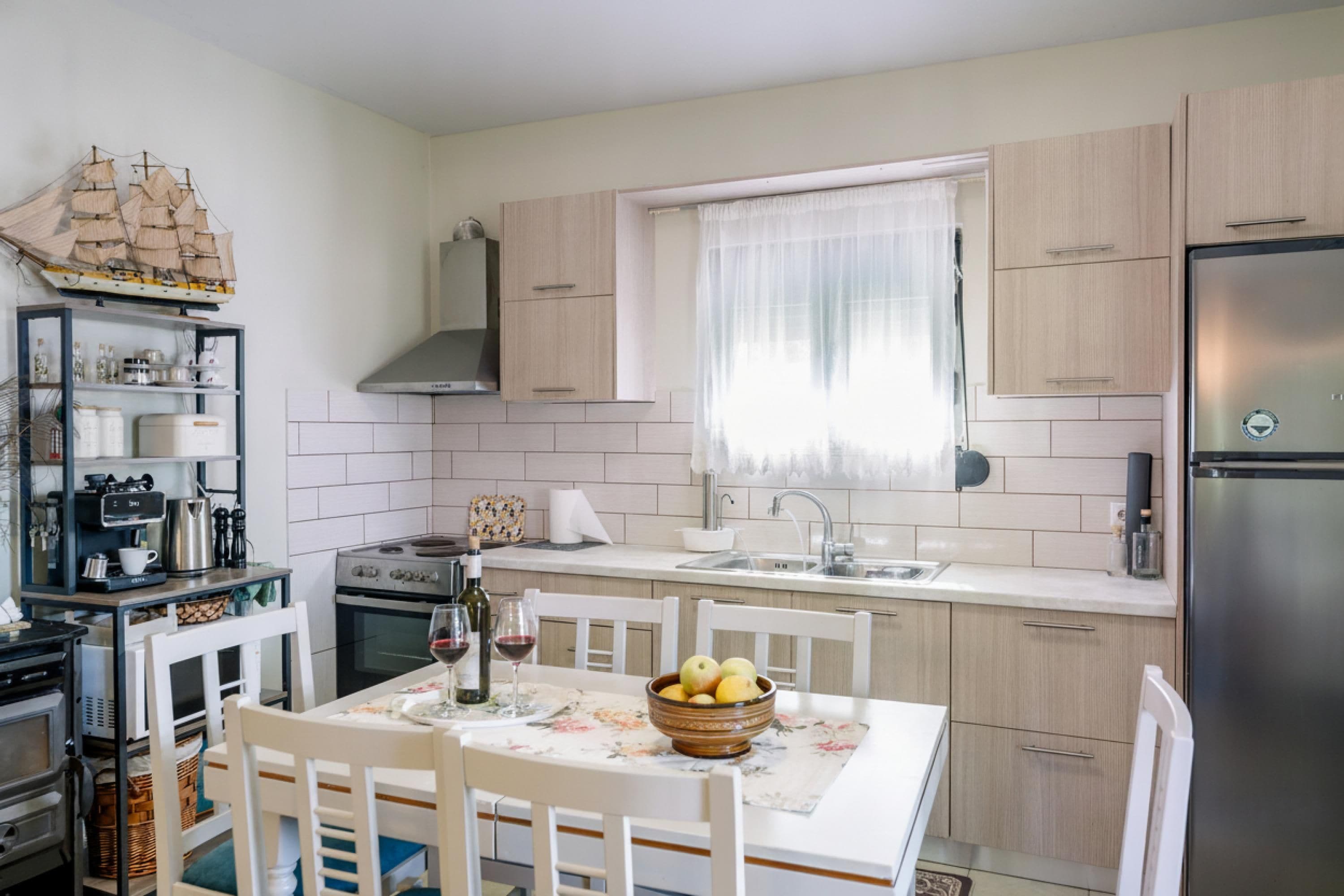 A compact kitchen with white cabinetry, a built-in oven, a stainless steel refrigerator, and a dining area with a table set for two.