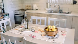 Cozinha com mesa de jantar posta, toalha de mesa florida, tigela de frutas e copos de vinho.
