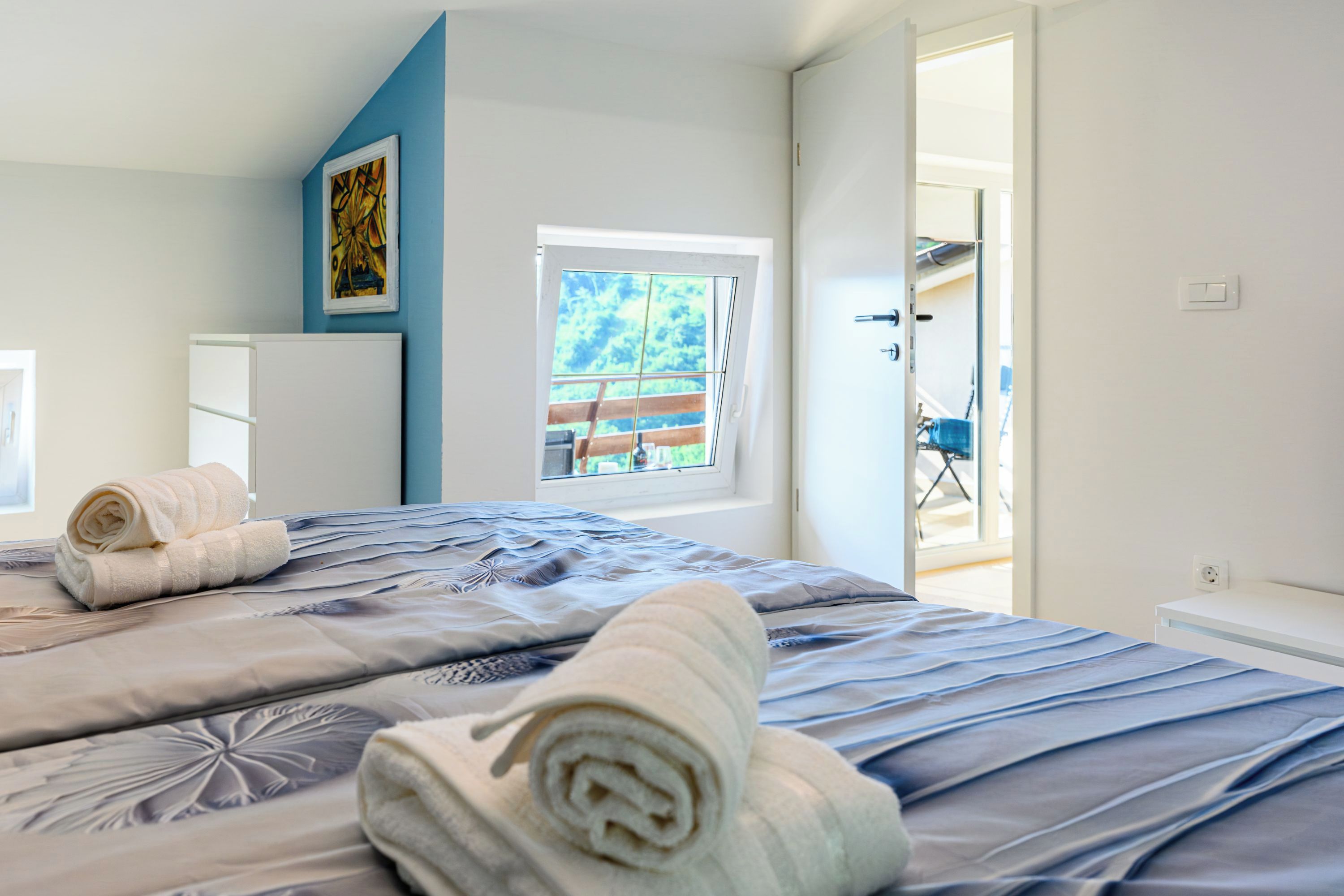 Camera d'albergo con un letto, una finestra, una porta che dà su uno spazio esterno e un'opera d'arte appesa al muro.