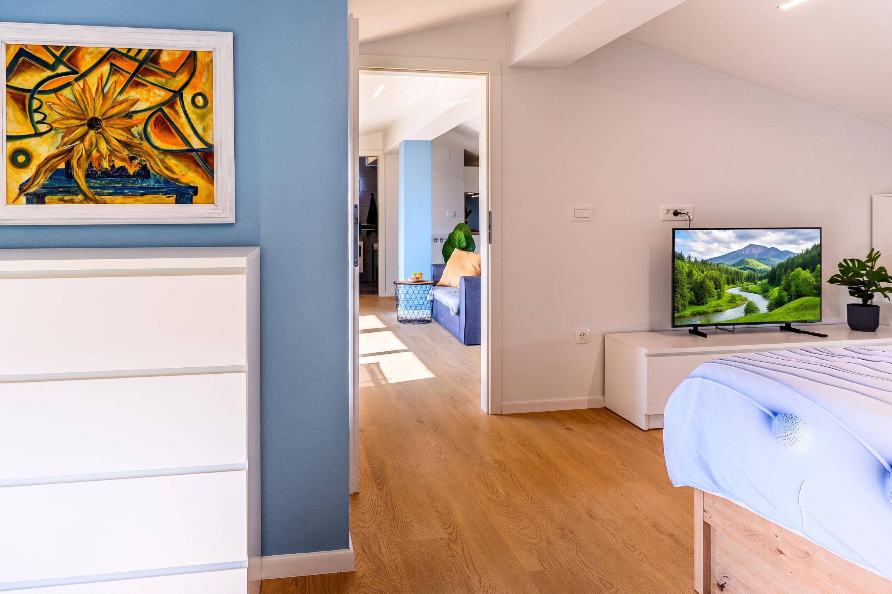 A modern bedroom with a bed, a television, and a painting on the wall.