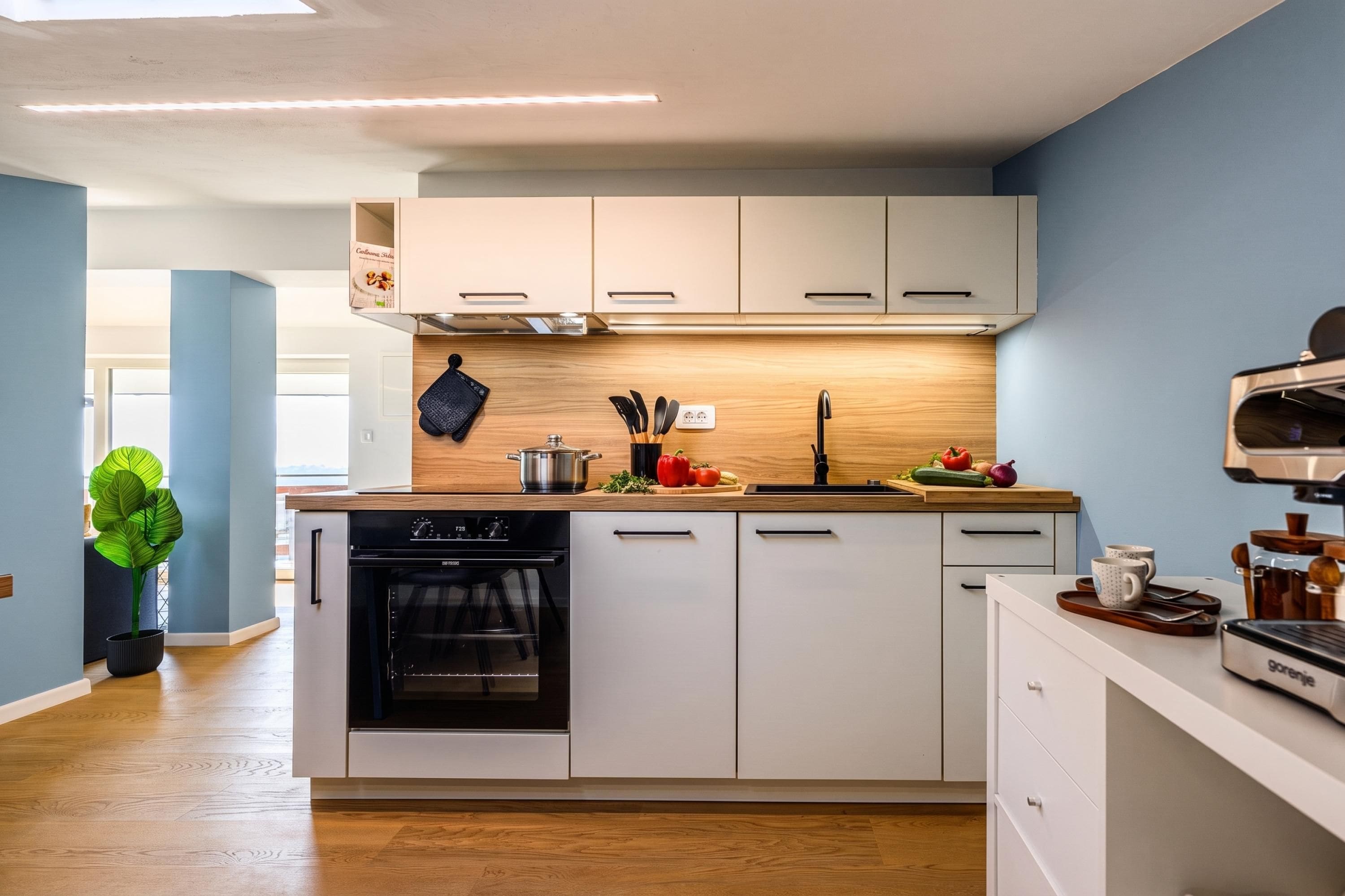 A modern kitchen with white cabinets, a built-in oven, and a coffee machine.