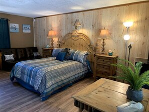Ein Schlafzimmer mit hölzernem Kopfteil, einem Bett mit gemusterten Textilien, zwei Nachttischen mit Lampen, einer Holzbank und einem Blumentopf.
