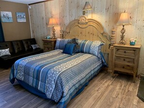 Ein Schlafzimmer mit einem hölzernen Kopfende, einer gemusterten Bettdecke, zwei Nachttischlampen und einem Nachttisch mit einer Vase.