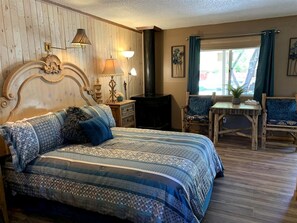 Ein Schlafzimmer mit Bett, Nachttischlampen, einem hölzernen Kopfteil, einem kleinen Tisch und Stühlen.
