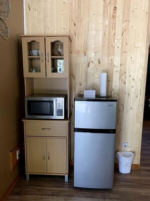 Eine Küchenzeile mit einer Mikrowelle, einem Kühlschrank und einem Holsschrank mit Glastüren.