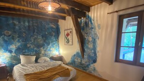 Une chambre à coucher avec un lit, un plancher en bois, une fenêtre et un mur orné d’un motif abstrait bleu.