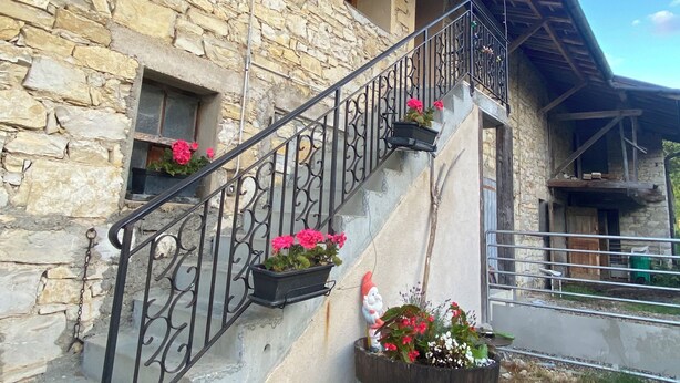 Un bâtiment en pierre doté d’un escalier, d’une rampe en métal et de jardinières.