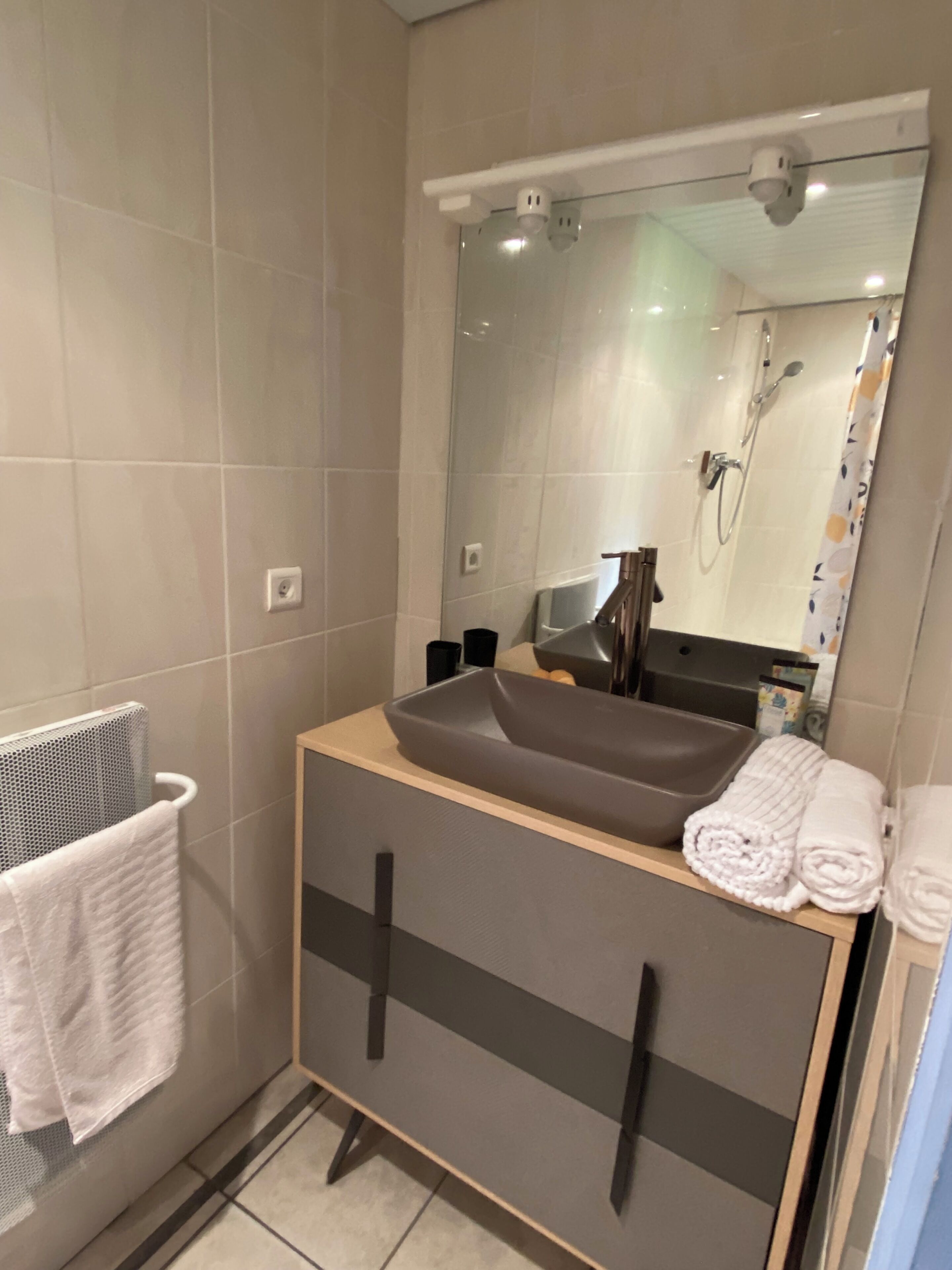 Ein Badezimmer mit Waschbecken, Spiegel, Handtuchhalter und Dusche.