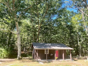 Une petite cabane en bois avec une porte rouge, entourée d’une forêt dense.