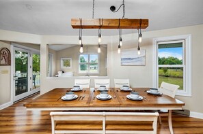 A dining room with a wooden table set for six, white chairs, and a view of the outdoors through large windows. - Design Cabin with Jacuzzi and Porch in Sister Bay, Wisconsin (Sister Bay)