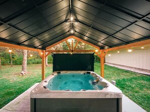 A hot tub under a covered area with a metal roof, surrounded by a grassy yard and trees. - Design Cabin with Jacuzzi and Porch in Sister Bay, Wisconsin (Sister Bay)