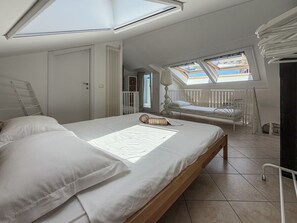 Ein Schlafzimmer mit Dachfenster, einem Bett, einer Leiter und einem Fenster.