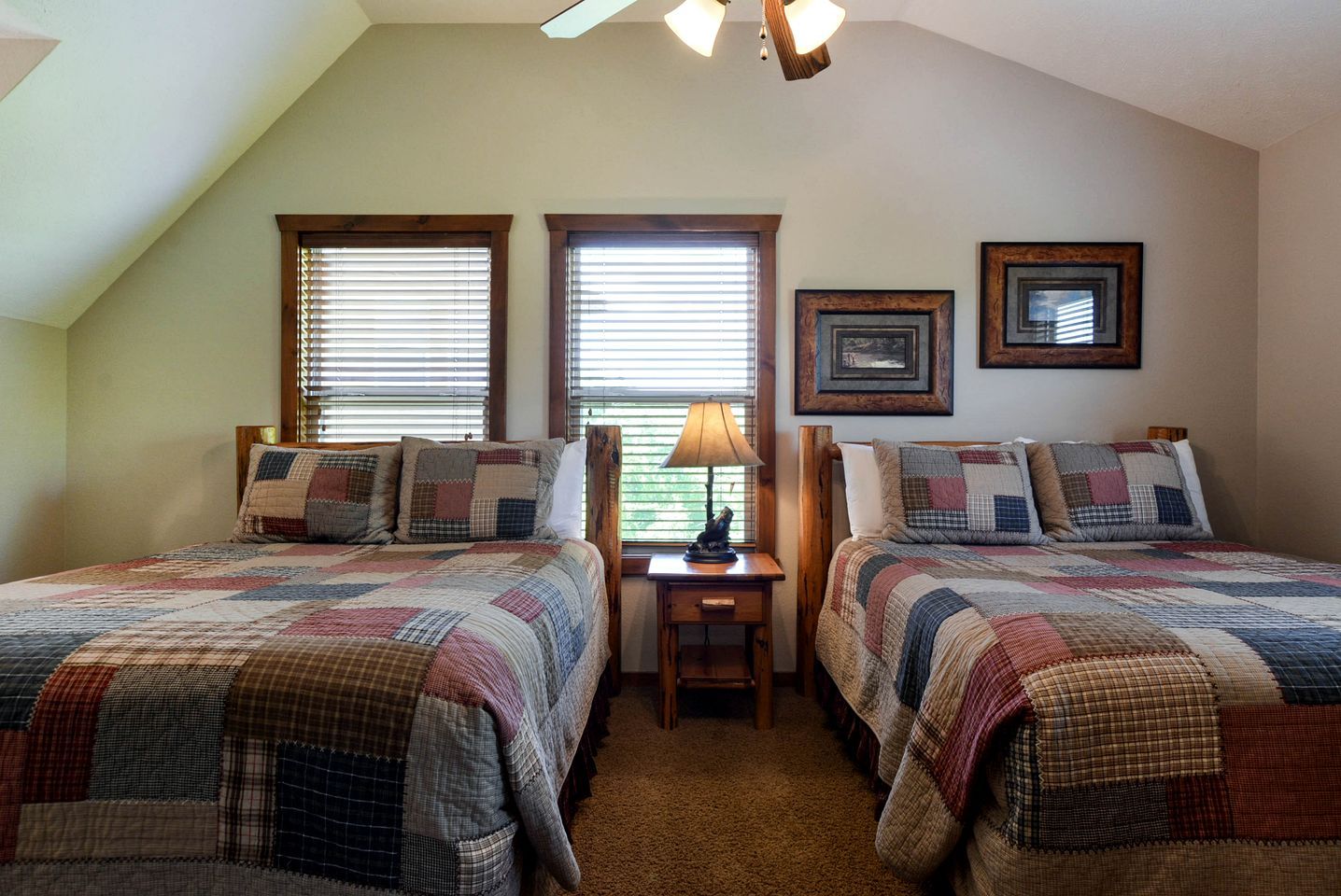 A bedroom with two beds, a nightstand, a lamp, and two windows with blinds.