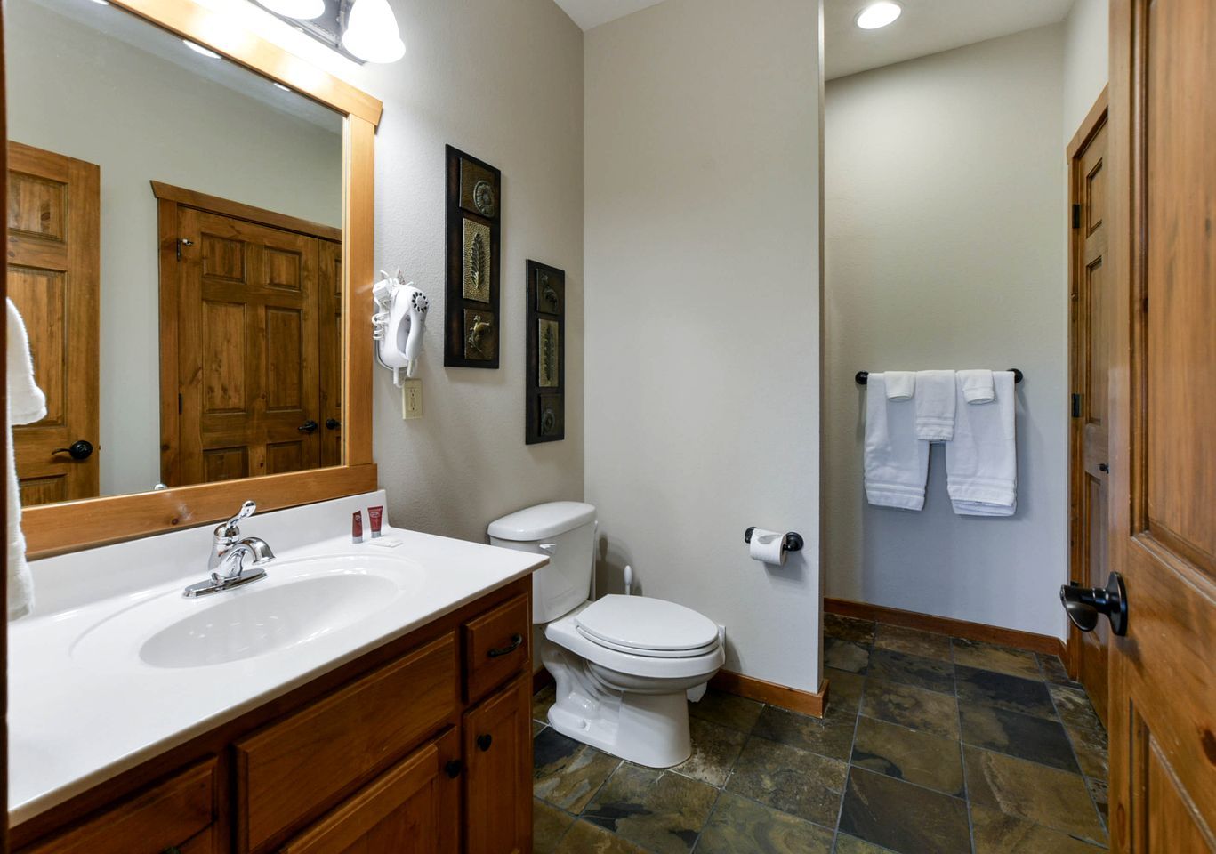 A bathroom with a white sink, wooden vanity, a toilet, and a shower area.